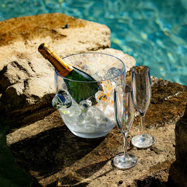 Revel Champagne flutes and a champagne bottle on a rocky outcropping beside a pool