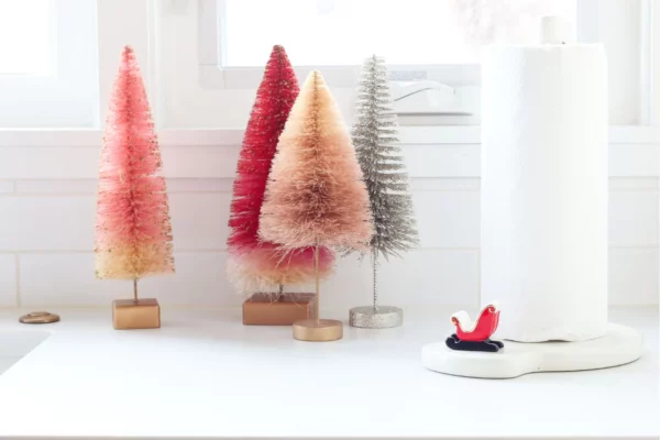 Nora Fleming Mini Sleigh attached to a paper towel holder next to decorative trees