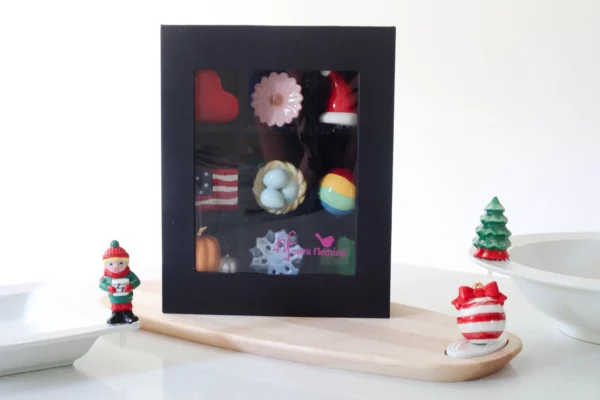 Nora Fleming Mini Fa la la Caroler with other holiday themed minis next to the keepsake box