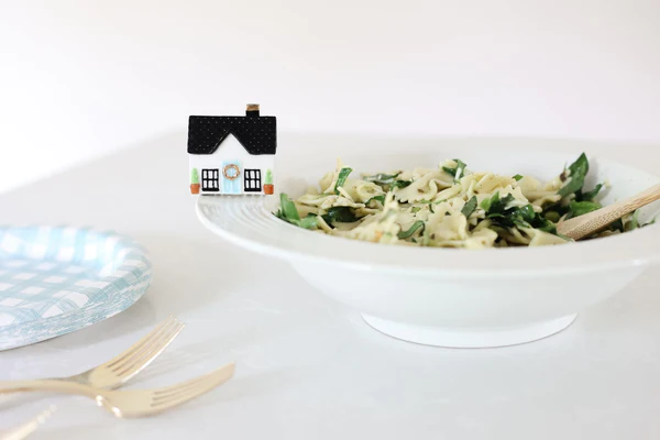 Nora Fleming Mini Home Sweet Home pictured attached to a bowl fille with bowtie pasta