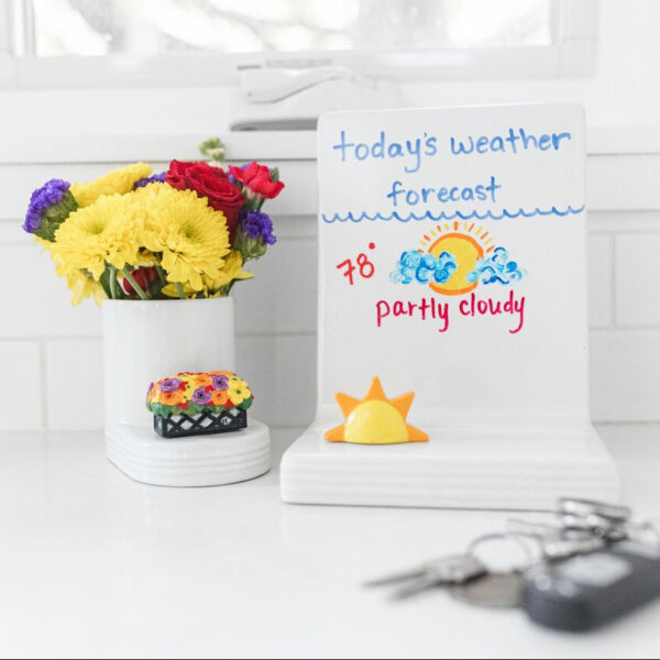 Nora Fleming message board base with a drawing of today's weather forecast. Pictured with the Here Comes the Sun mini and the Love Blooms Here mini.